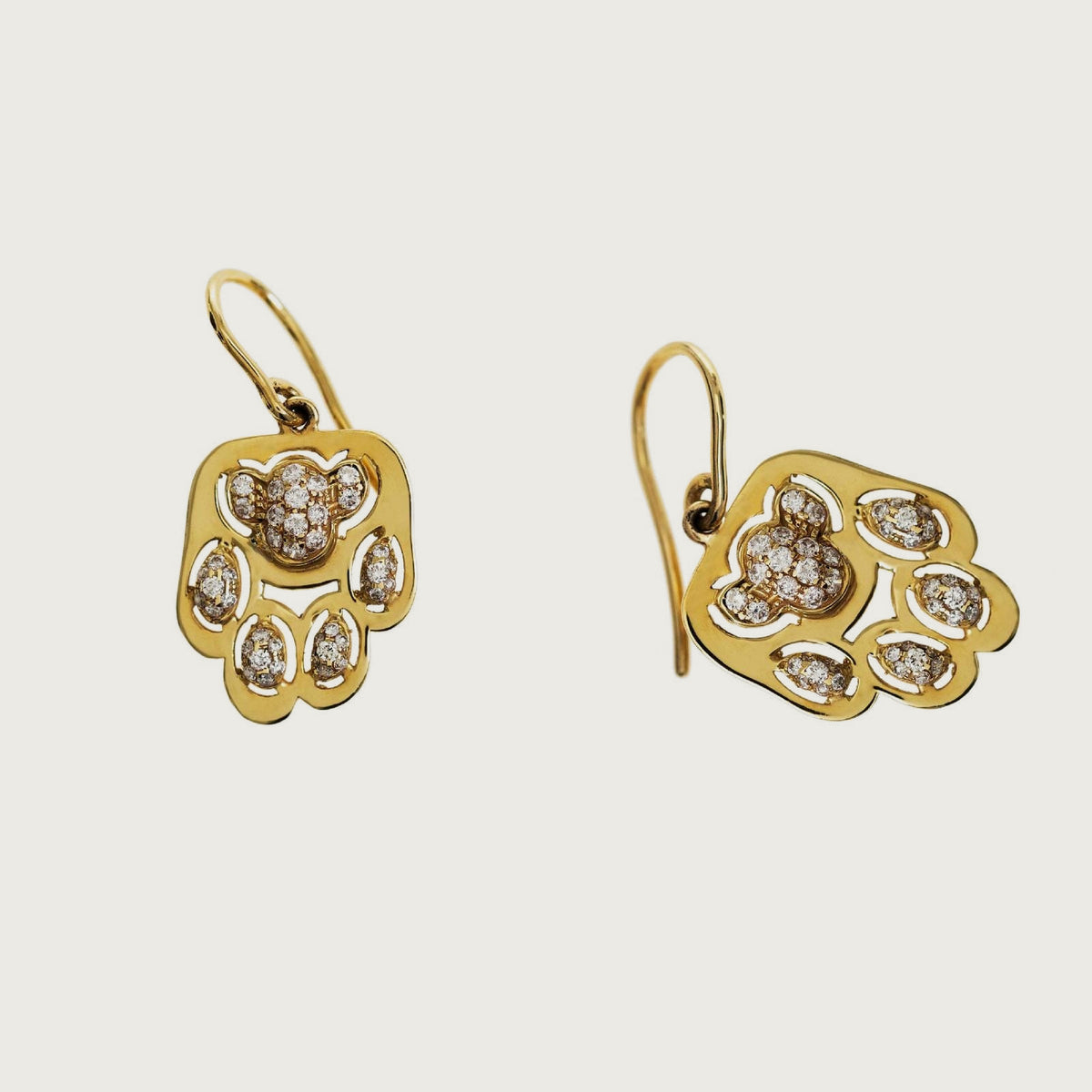 Vibrisse earrings in yellow gold with white diamonds, on French hooks, on a bone-white background.
