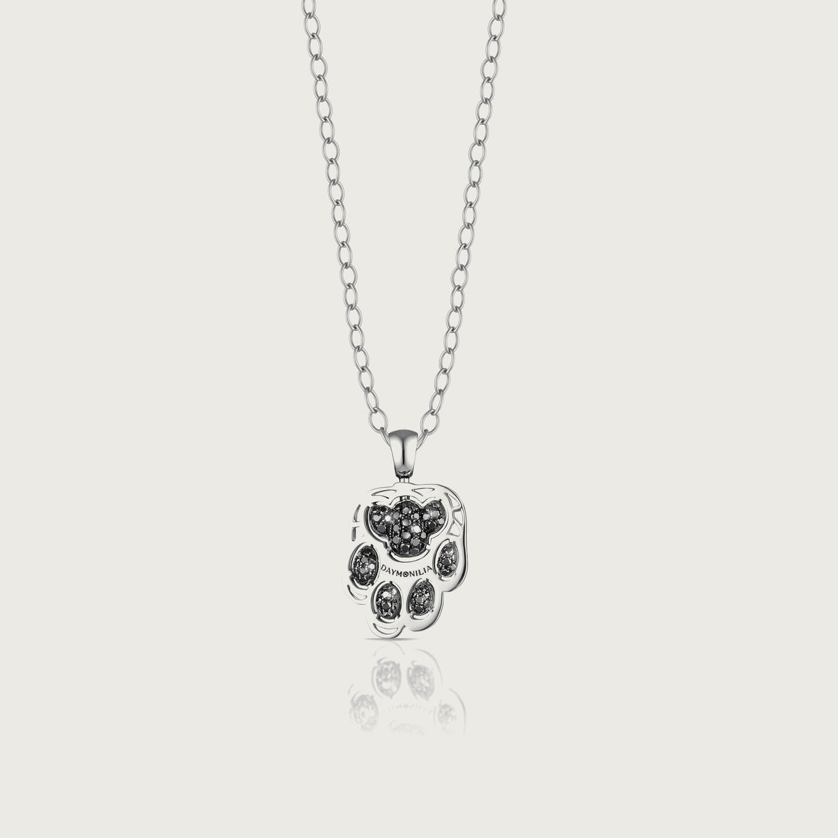 Pardo, a white gold paw pendant with 122 black diamonds, seen from the front on a bone-white background, the band engraved Daymonilia.