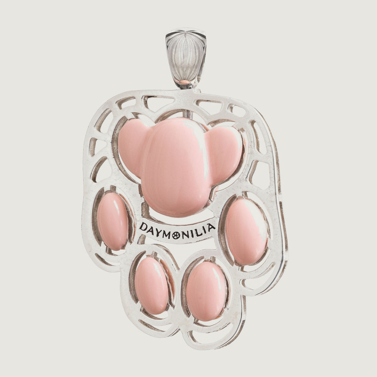 Palmo frontale su fondo osso: la zampa di Daymon in argento traforato, cinque cuscinetti rosa in composto vitreo e la fascia incisa Daymonilia.