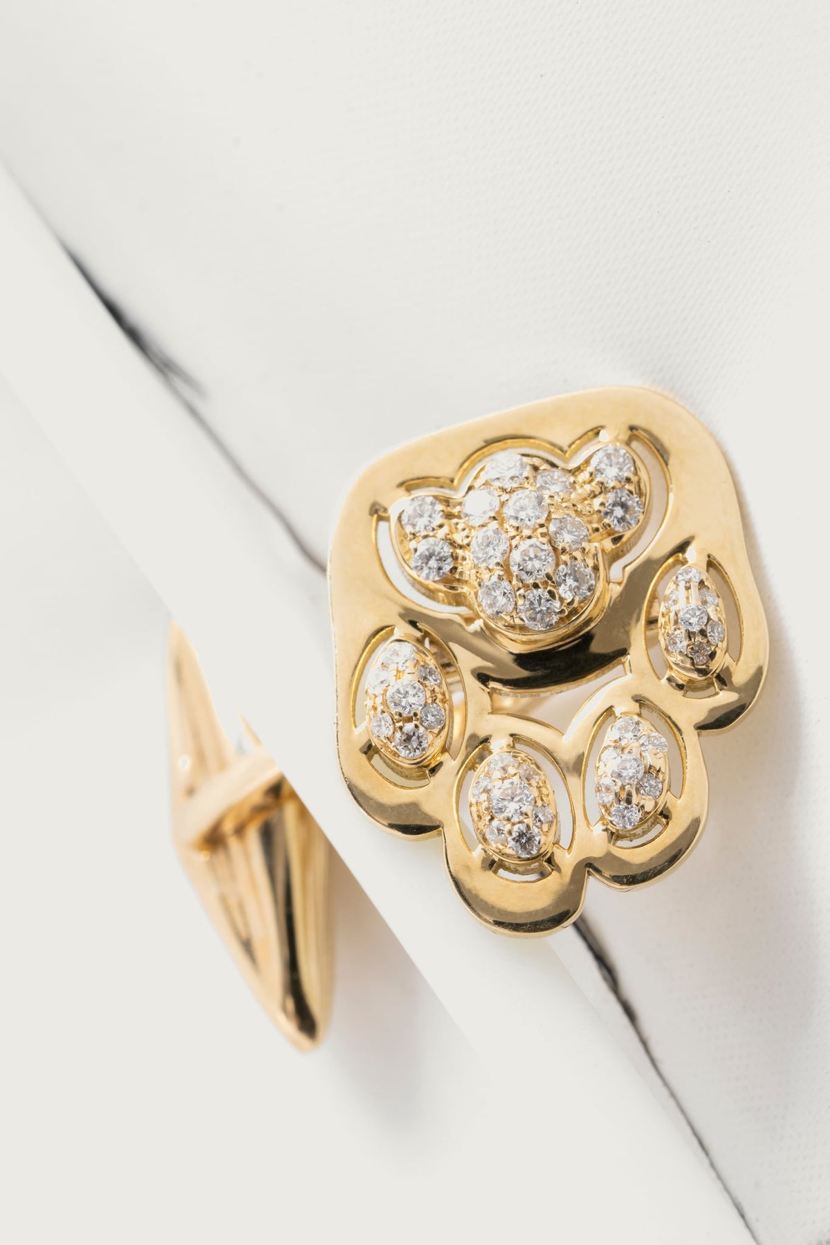Gemello Vibrisse in oro giallo con diamanti bianchi, posato su un piano di marmo bianco venato.