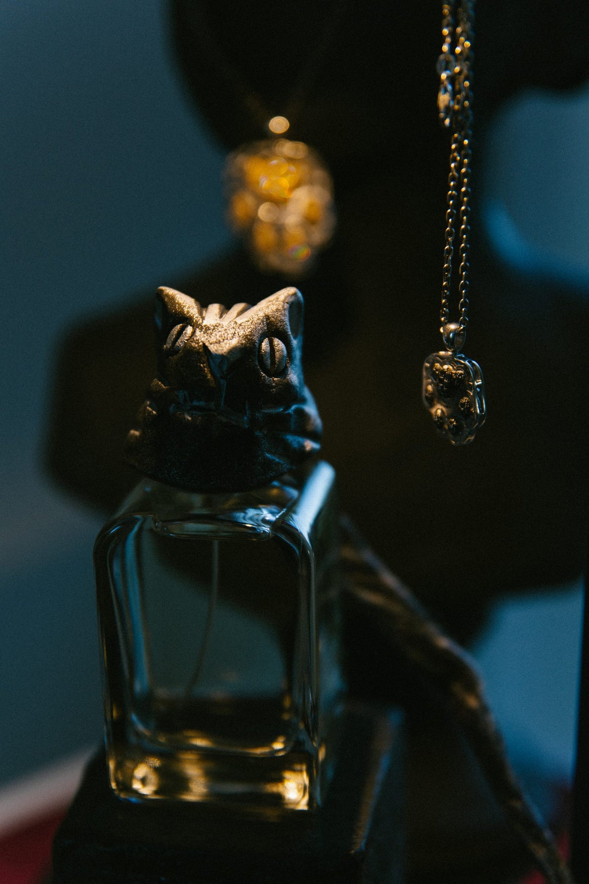 Il flacone del profumo Daymon, con la sua testa scolpita, e due pendenti della Felide appesi nella penombra.