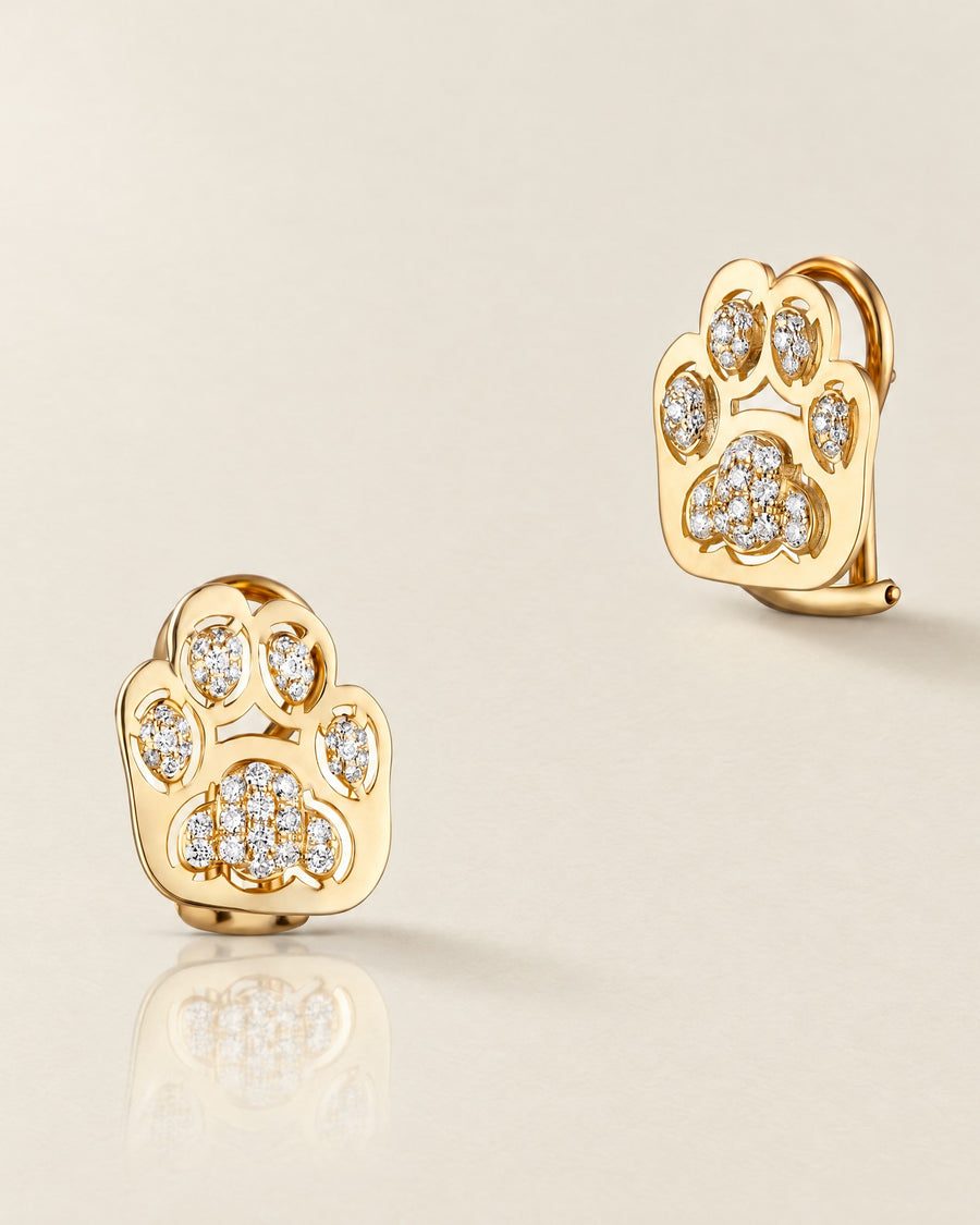 The Vibrisse earrings in yellow gold with white diamonds and clip backs, on a bone-white ground.